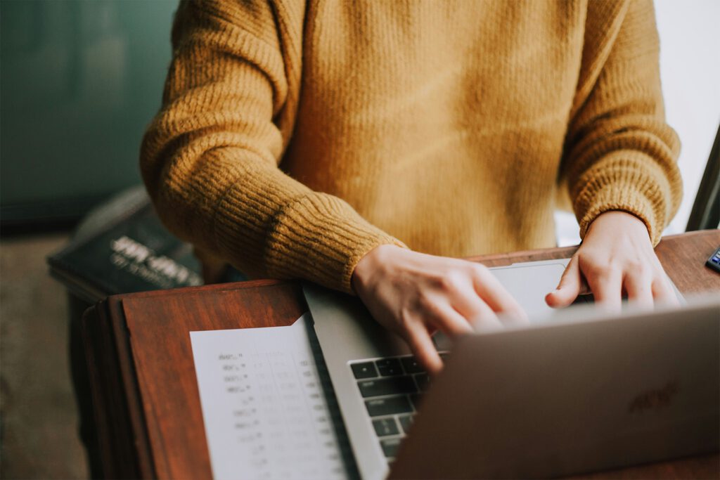 Person arbeitet an Laptop mit Taschenrechner und gedruckten Tabellen, Onlinekurse zu Preisrecht und Zuwendungsrecht